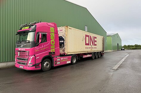 Pinkfarbener Glomb Elektro Lkw mit ONE Container an Lagerhalle