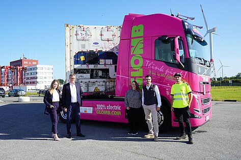 Team vor pinkfarbenem Glomb Elektro Lkw mit Kühlcontainer